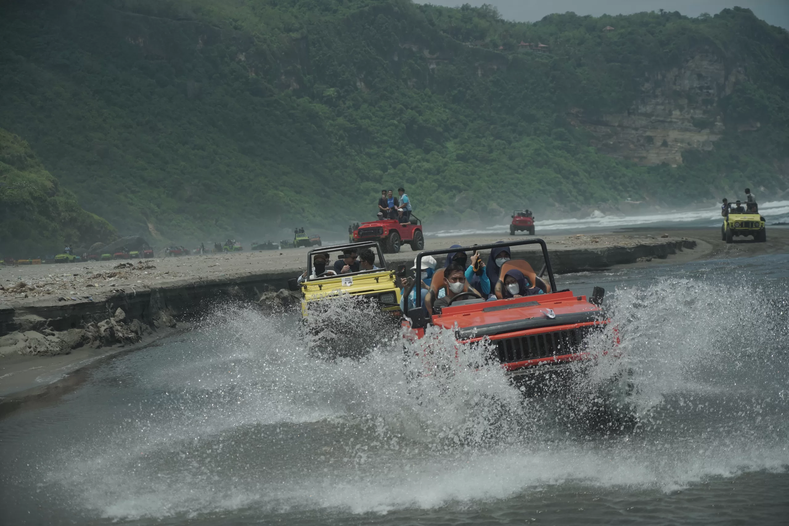 Students riding an open-top jeep through shallow coastal water