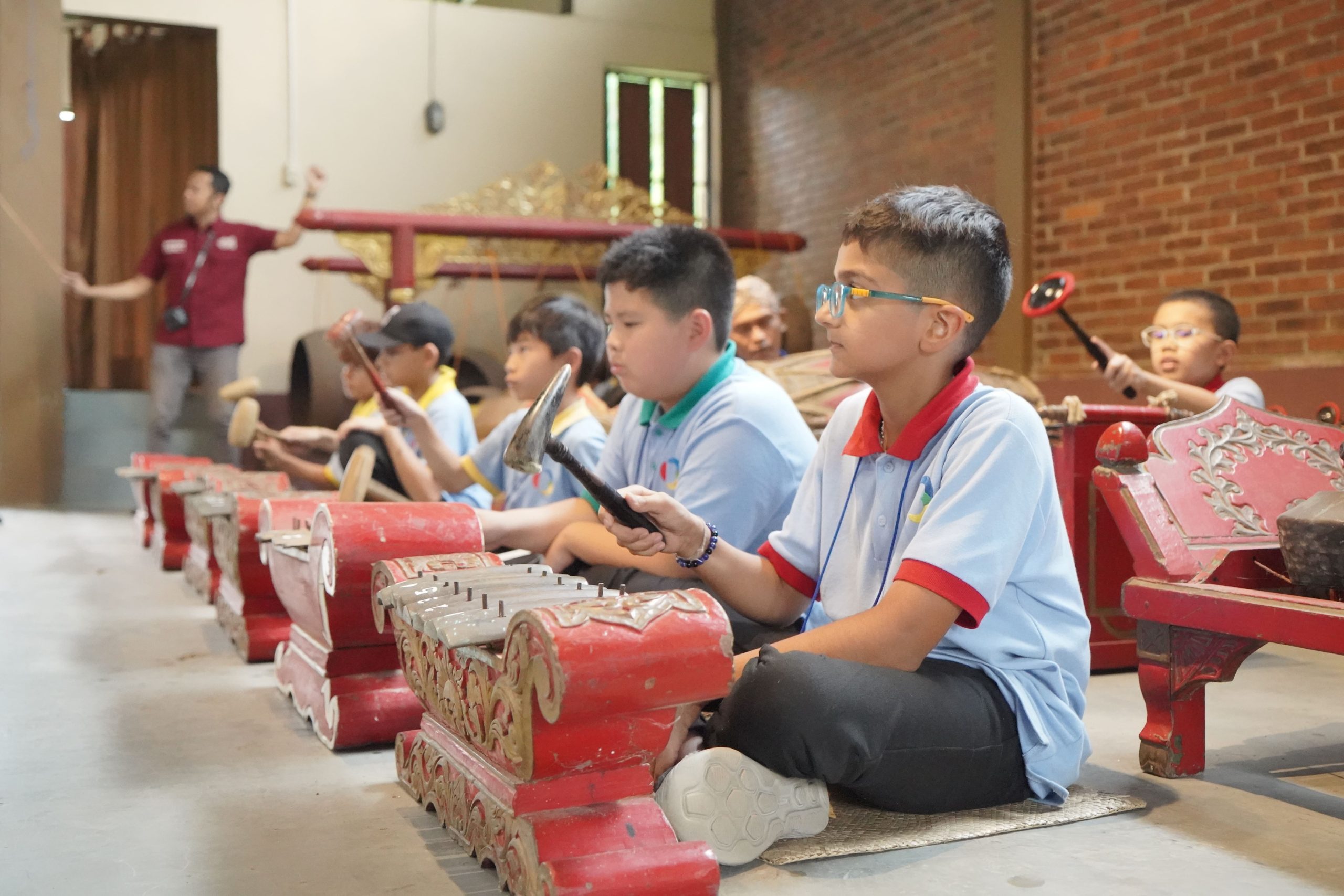 Students playing traditional Javanese gamelan instruments, guided by a facilitator